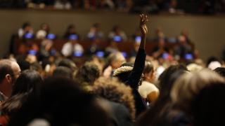 full auditorium and someone has their hand in the air.