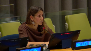 Maria Noel Leoni is seated at the panel behind her name sign, addressing the event