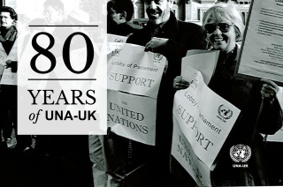 Black and white photo of UNA-UK campaigners standing in a line holding posters reading 'lobby of parliament, support the United Nations'